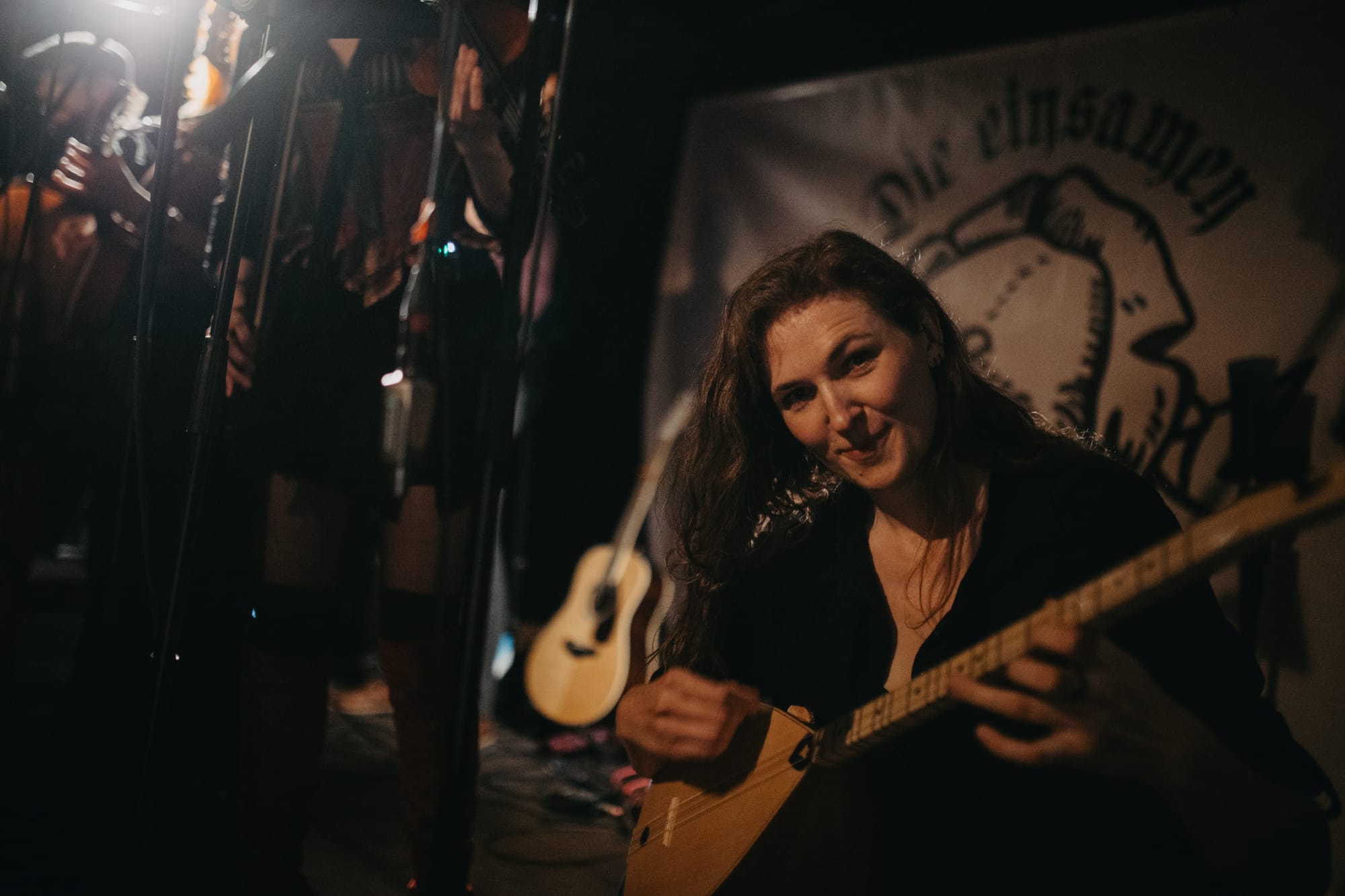 A woman playing turkish lute looking directly into the camera and smirking.