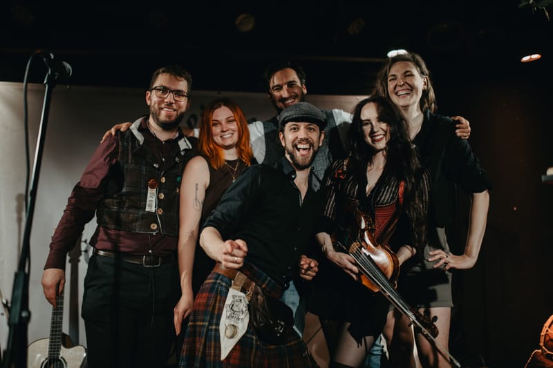 Our six musicians smiling euphorically and hugging one another.